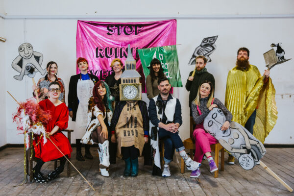Members of Array Collective pose in costumes including Big Ben, smiling, some are holding placards featuring a Sheela Na Gig